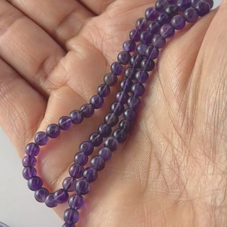 A video person holds delicate strands of Amethyst beads, showcasing their smooth round design and gentle shine.