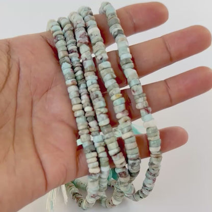 A video person holds delicate strands of Larimar beads, showcasing their smooth wheel design and sparkle.