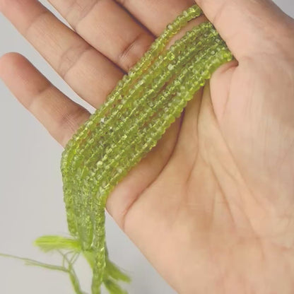 A person holds delicate strands of Peridot beads, showcasing their faceted rondelle design.