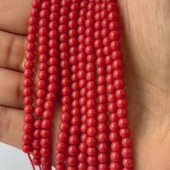 A person holds delicate strands of Taiwan Coral beads, showcasing their smooth design.