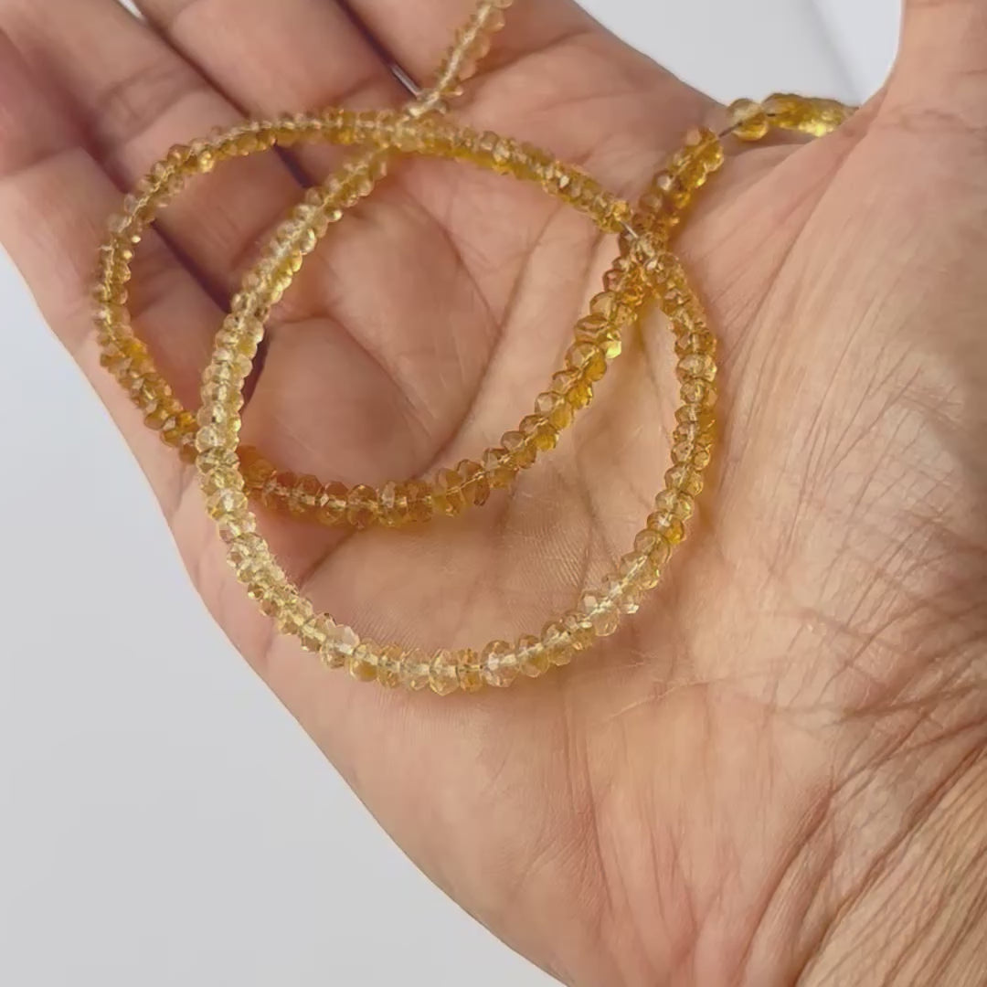 A video person holds delicate strands of Citrine beads, showcasing their faceted rondelle design and sparkle.
