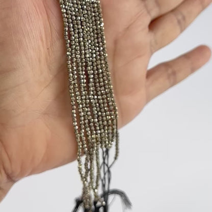 A person holds delicate strands of Pyrite beads, showcasing their smooth design.