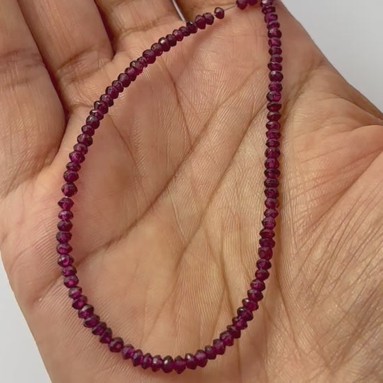 A person holds delicate strands of garnet beads, showcasing their faceted design.