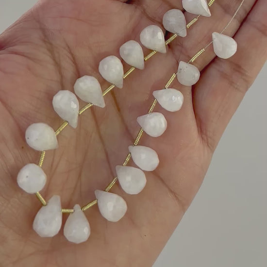 A person holds delicate strands of White Rainbow Moonstone beads, showcasing their faceted design.