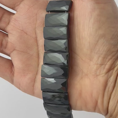 A video person holds delicate strands of Black Onyx beads, showcasing their faceted rectangle design and sparkle.