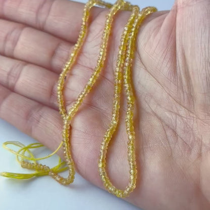 A video person holds delicate strands of Yellow Sapphire beads, showcasing their faceted rondelle design and sparkle.