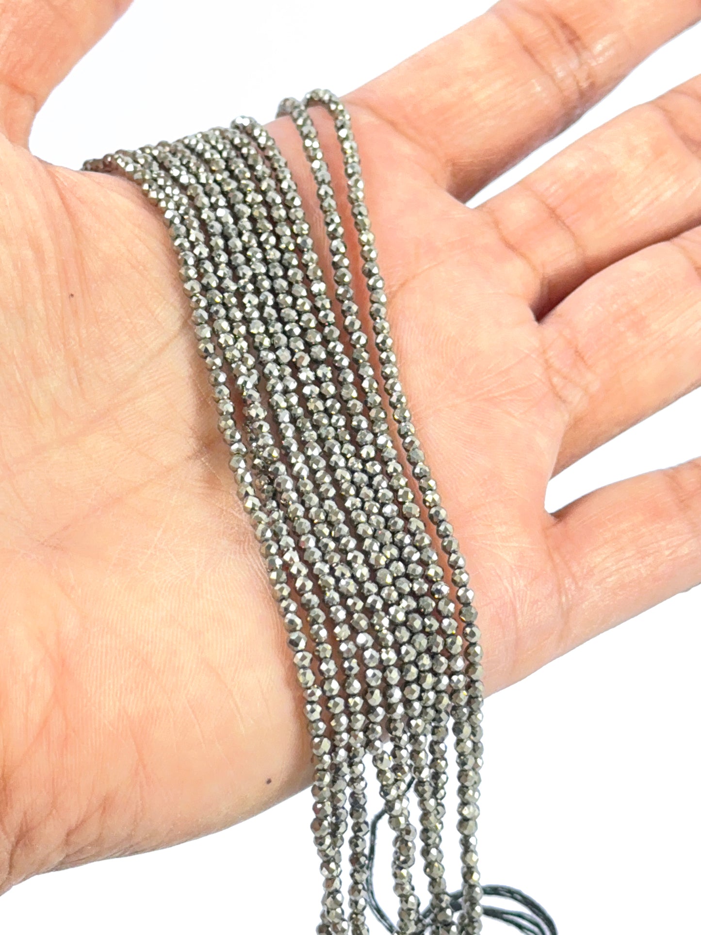 A person holds delicate strands of Pyrite beads, showcasing their smooth design.