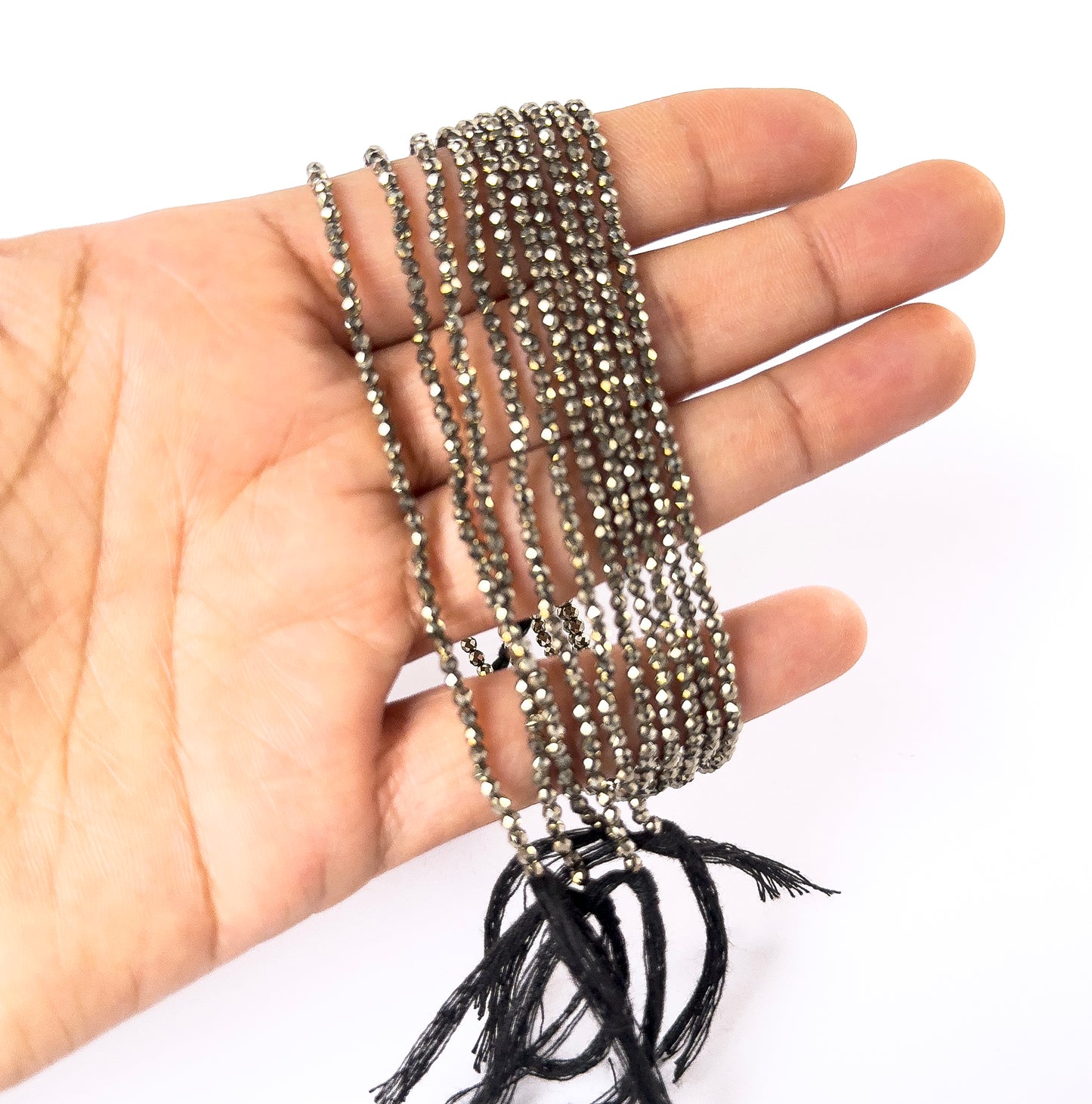 A person holds delicate strands of Pyrite faceted rondelle beads, showcasing their cut design.