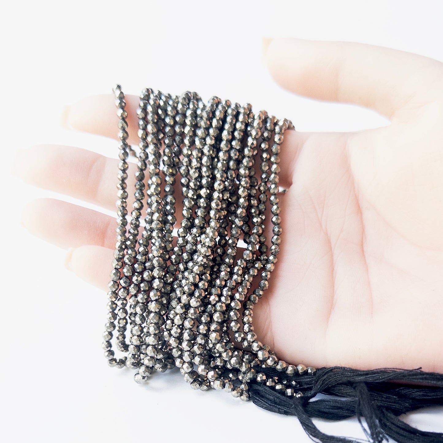 A person holds delicate strands of Pyrite beads, showcasing their faceted rondelle design.