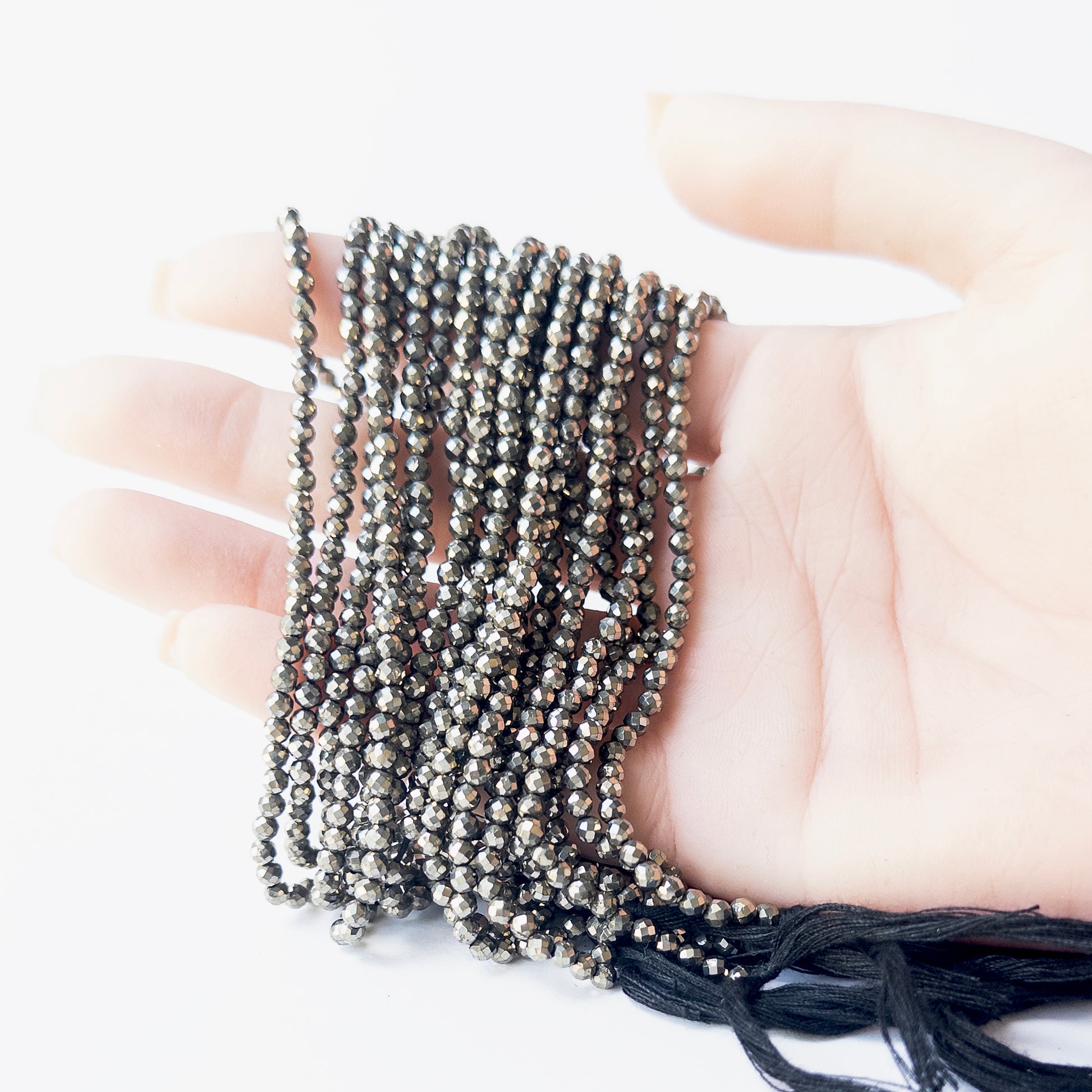 A person holds delicate strands of Pyrite beads, showcasing their faceted rondelle design.