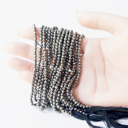 A person holds delicate strands of Pyrite beads, showcasing their faceted rondelle design.