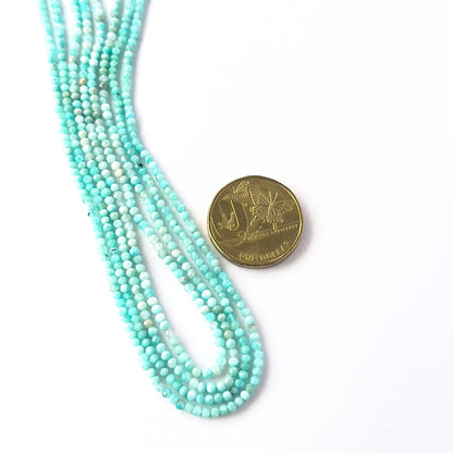 A coin is placed near delicate strands of Amazonite beads for scale.