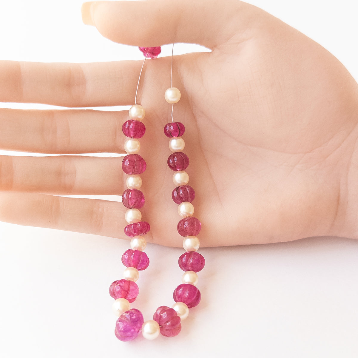 A person holds delicate strands of Quartz and Shell Pearl beads, showcasing their pumpkin‑cut design.