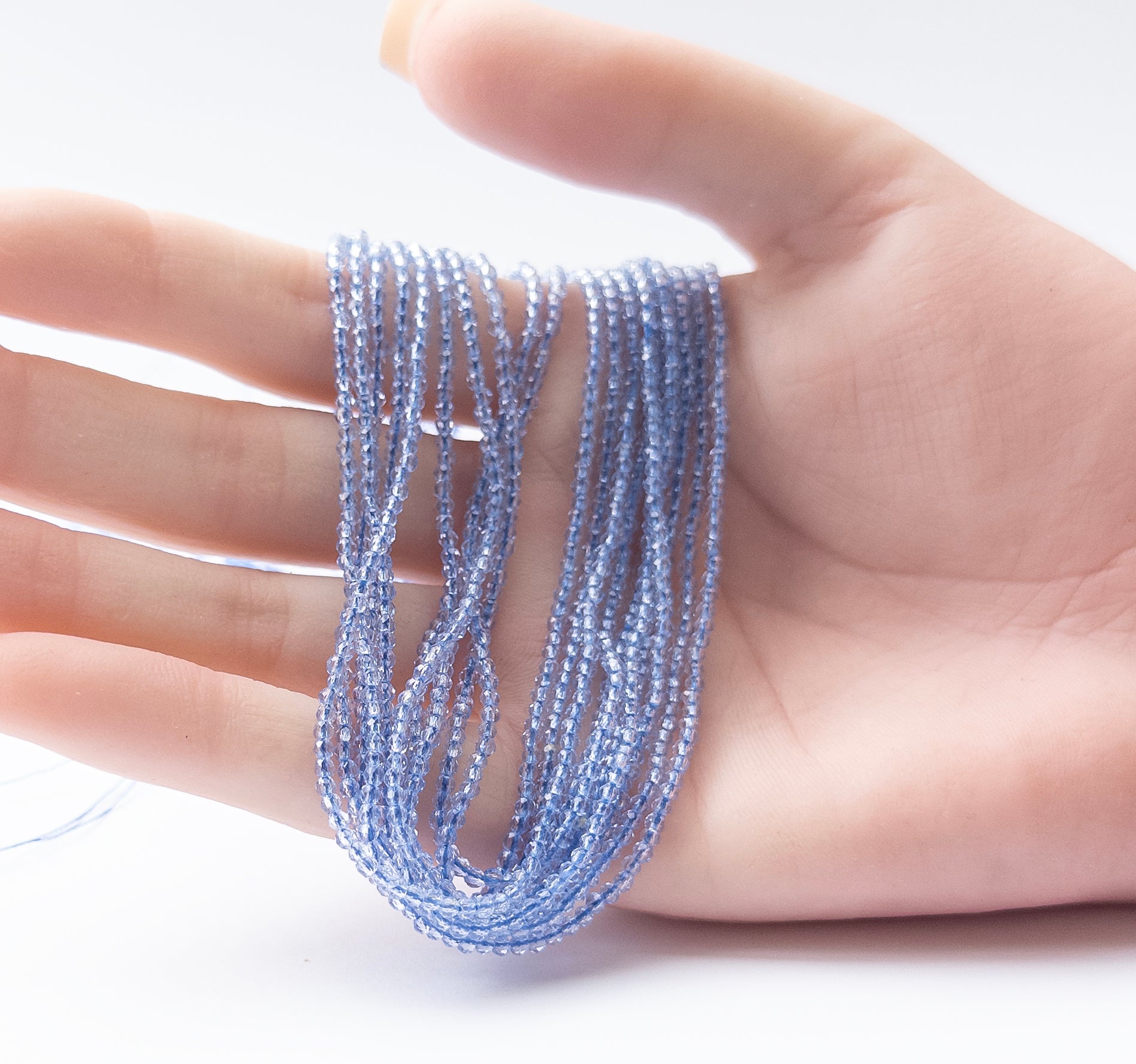 A person holds delicate pieces of Quartz faceted rondelle beads, showcasing their sparkle.