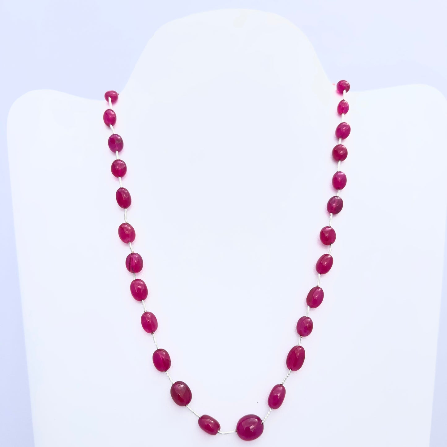 Quartz necklace with smooth oval beads in deep pink tones arranged on a white bust stand.