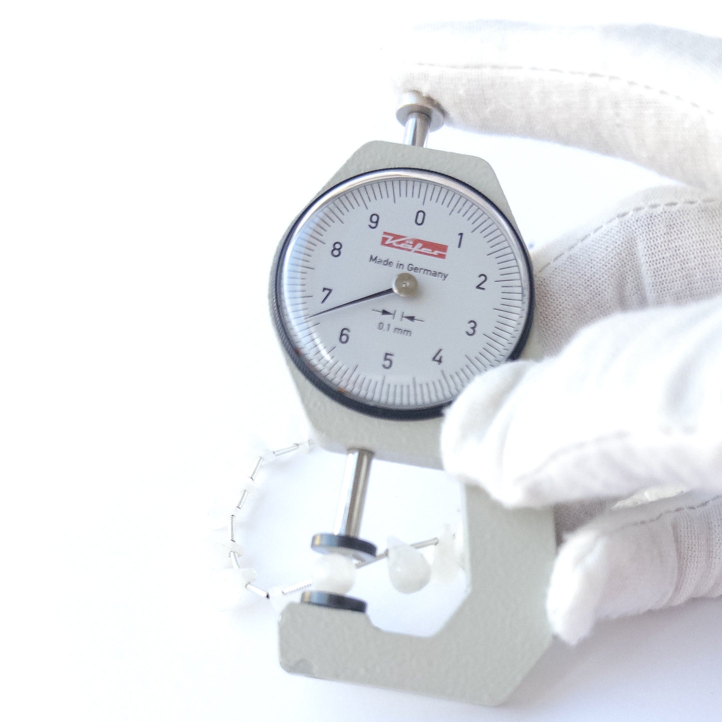 A dial gauge measures the Rainbow Moonstone faceted briolette 6.5–7mm gemstone.
