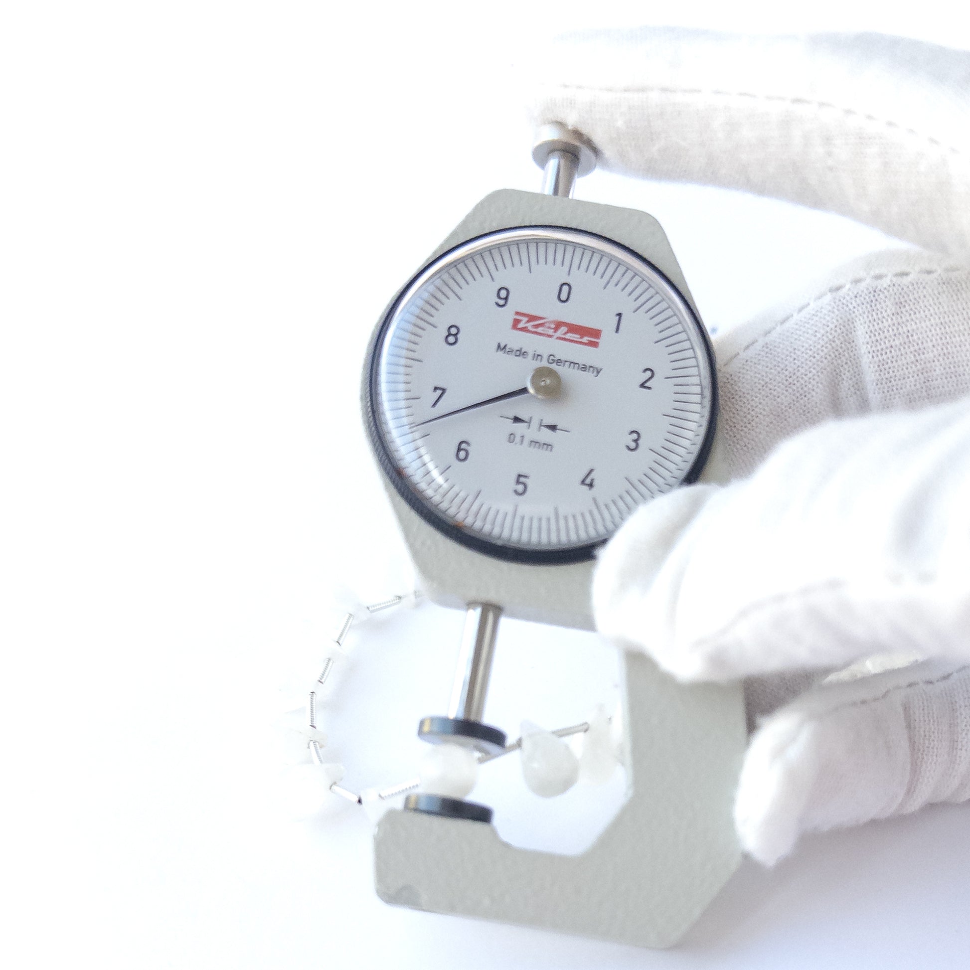 A dial gauge measures the Rainbow Moonstone faceted briolette 6.5–7mm gemstone.