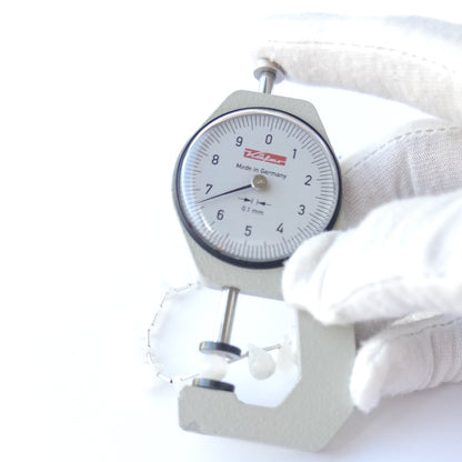 A dial gauge measures the Rainbow Moonstone faceted briolette 6.5–7mm gemstone.
