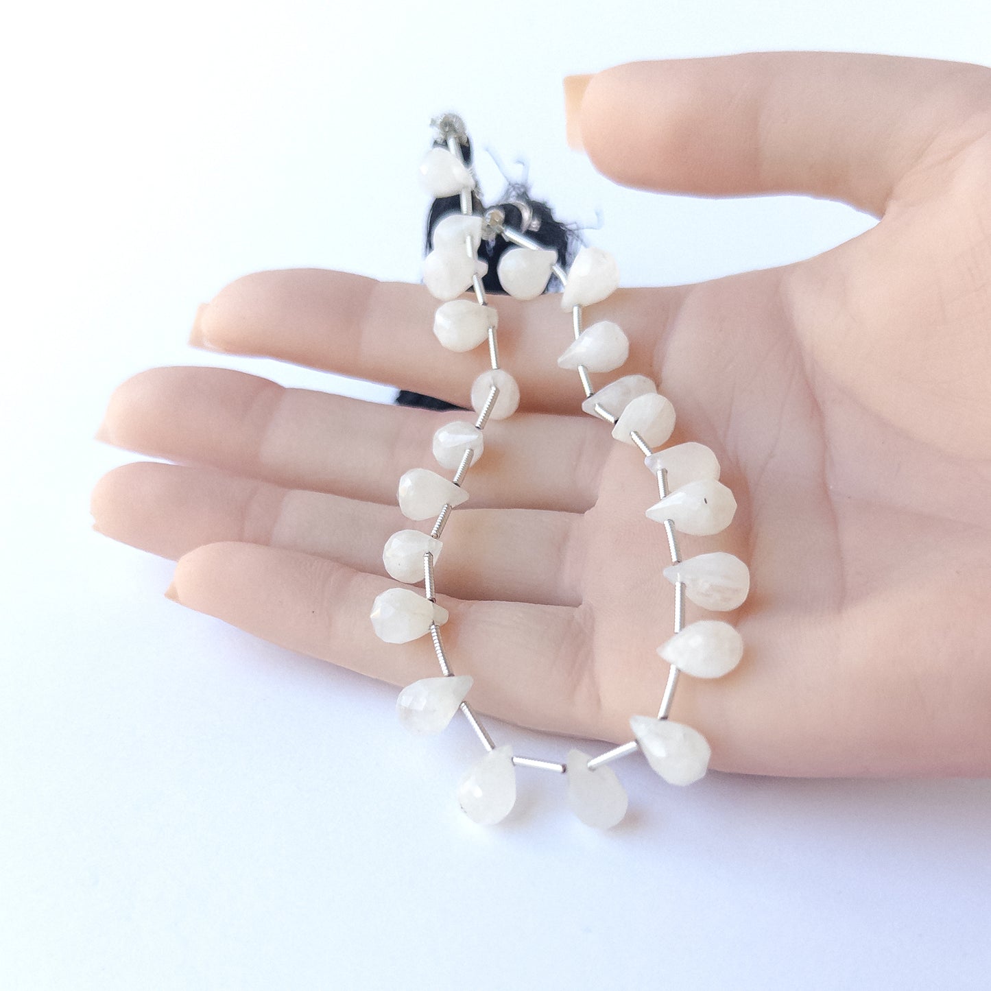 A person holds delicate pieces of Rainbow Moonstone beads, showcasing their faceted briolette design.
