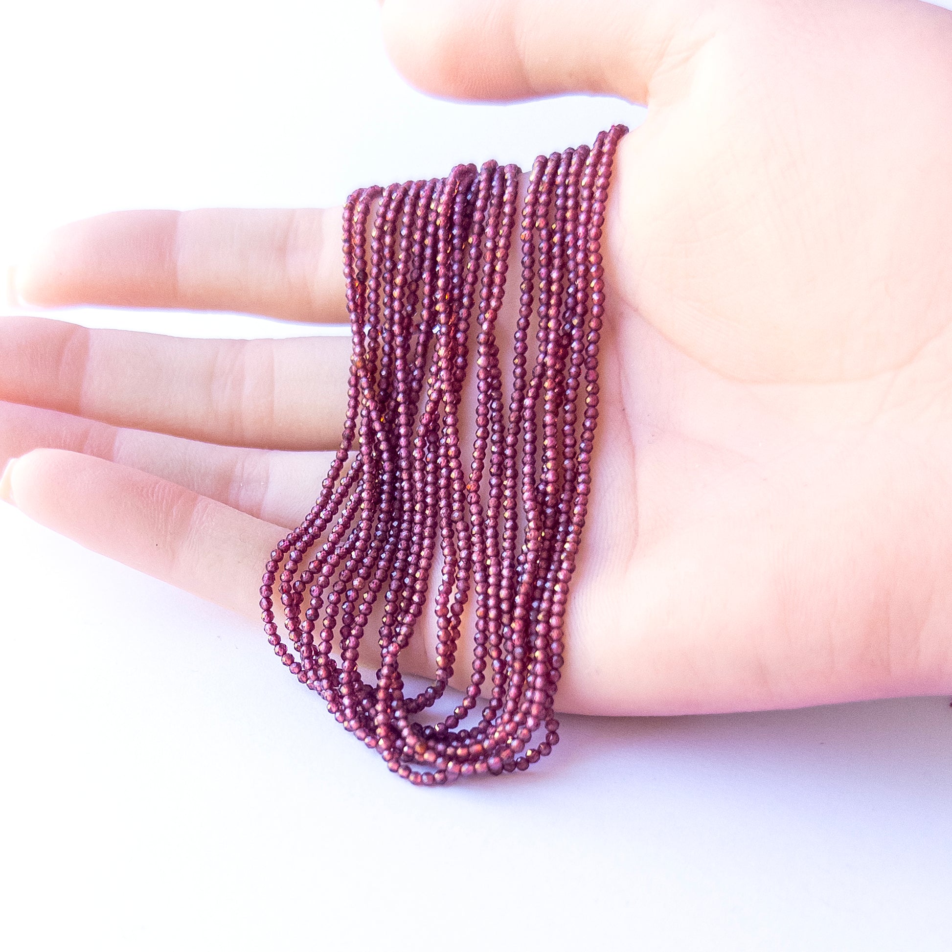 A person holds delicate strands of Rhodolite Garnet beads, showcasing their faceted rondelle design.