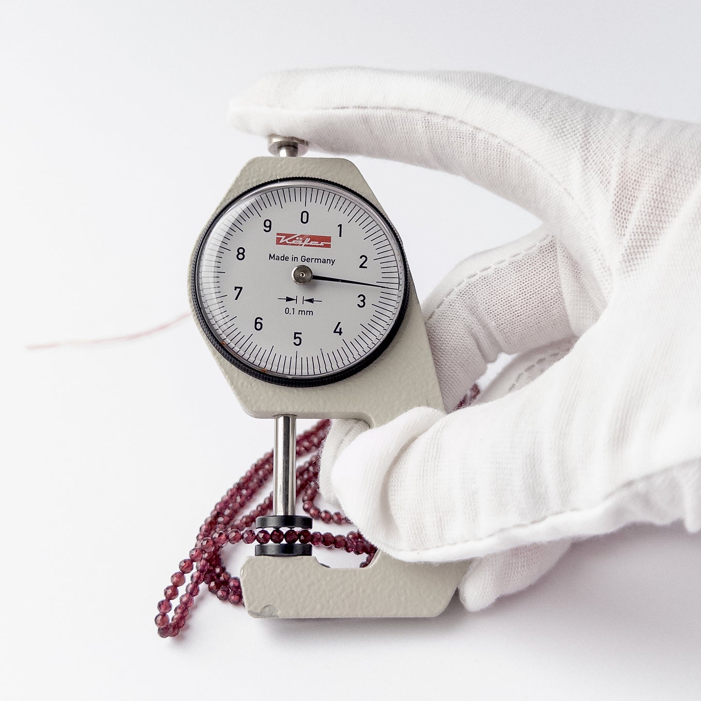 A dial gauge measures the Rhodolite Garnet faceted rondelle 2.7mm gemstone.