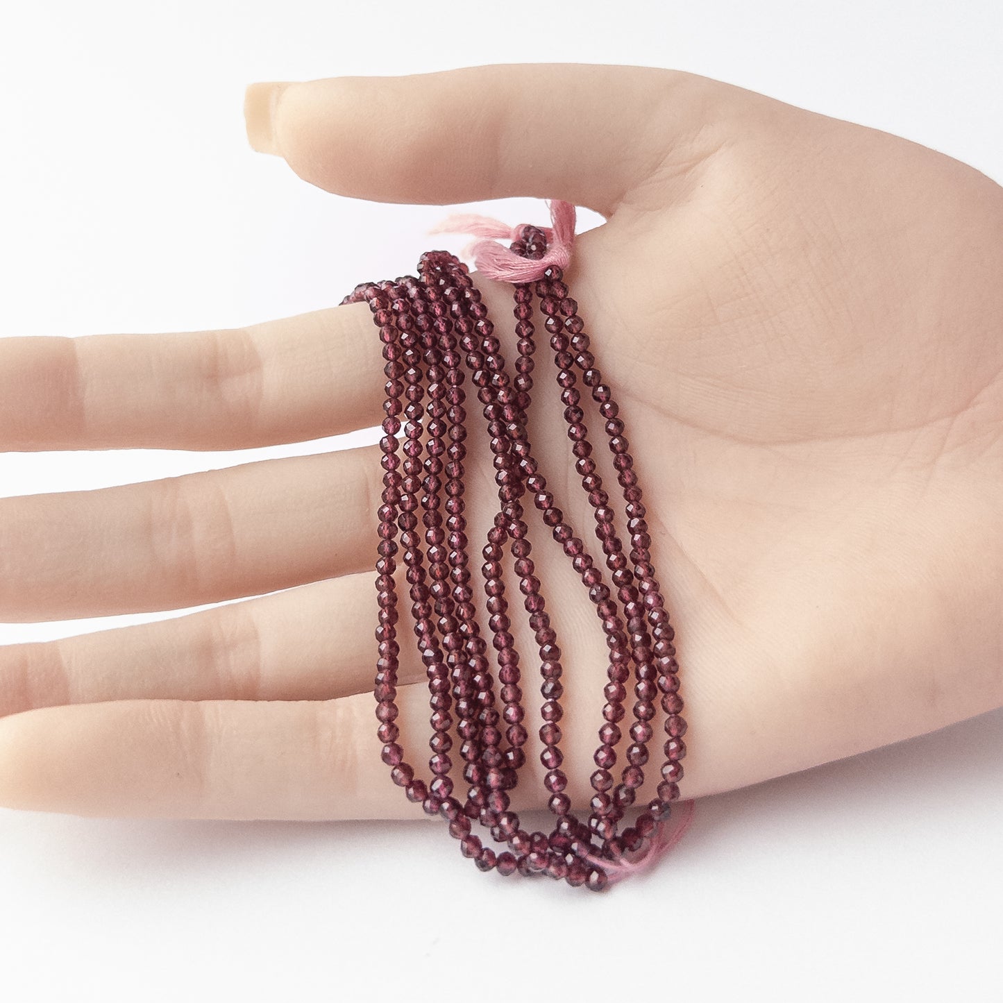 A person holds delicate strands of Rhodolite Garnet beads, showcasing their faceted rondelle design.