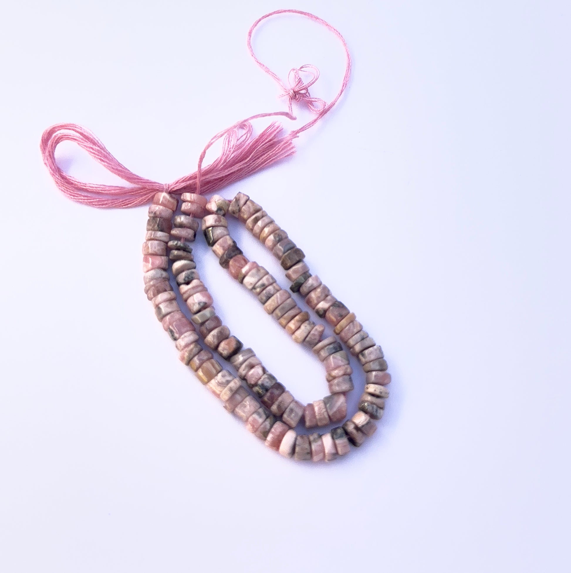 Close‑up of pink Rhodonite stone beads showing smooth wheel cuts and natural patterns.
