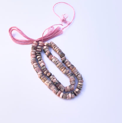 Close‑up of pink Rhodonite stone beads showing smooth wheel cuts and natural patterns.

