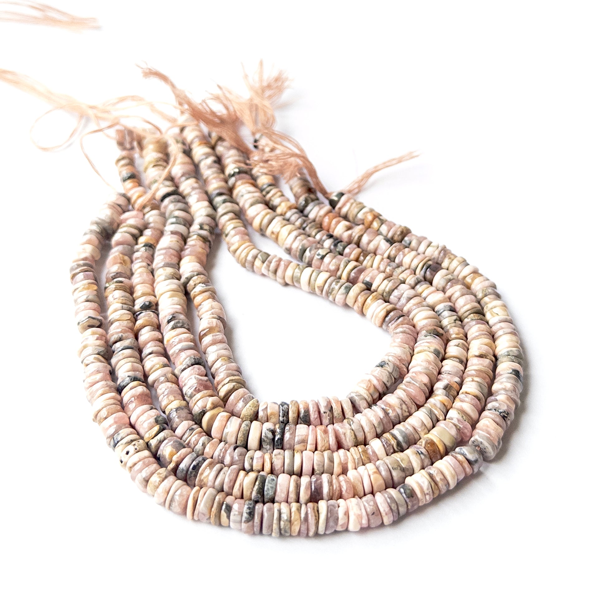 Rhodonite smooth wheel heishi gemstone beads arranged in a strand showing soft pink tones and polished finish.