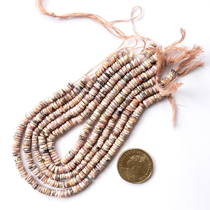 A coin is place near delicate strands of Rhodonite beads for scale.