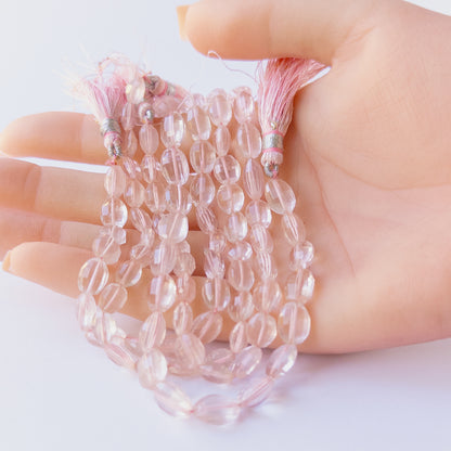 A person holds delicate strands of Rose Quartz beads, showcasing their faceted oval design.