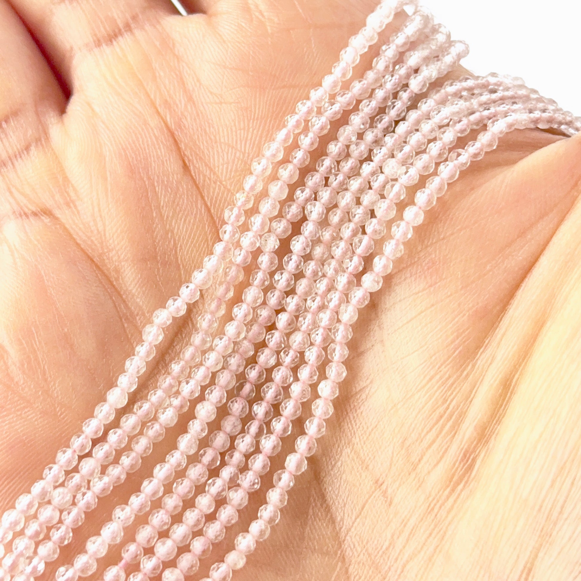 A person holds delicate strands of Rose Quartz beads, showcasing their faceted rondelle design.