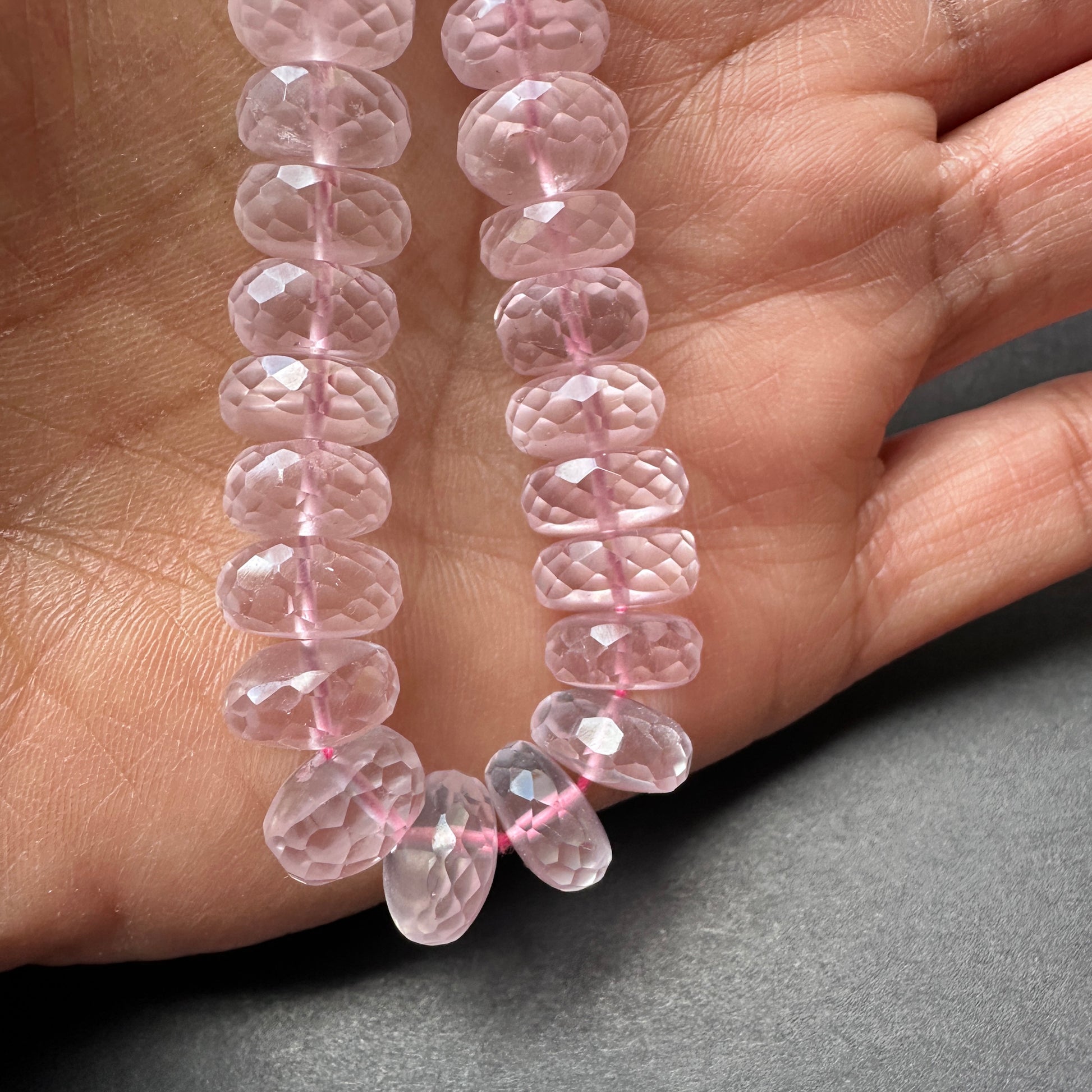 A person holds delicate strands of Rose Quartz beads, showcasing their smooth design.