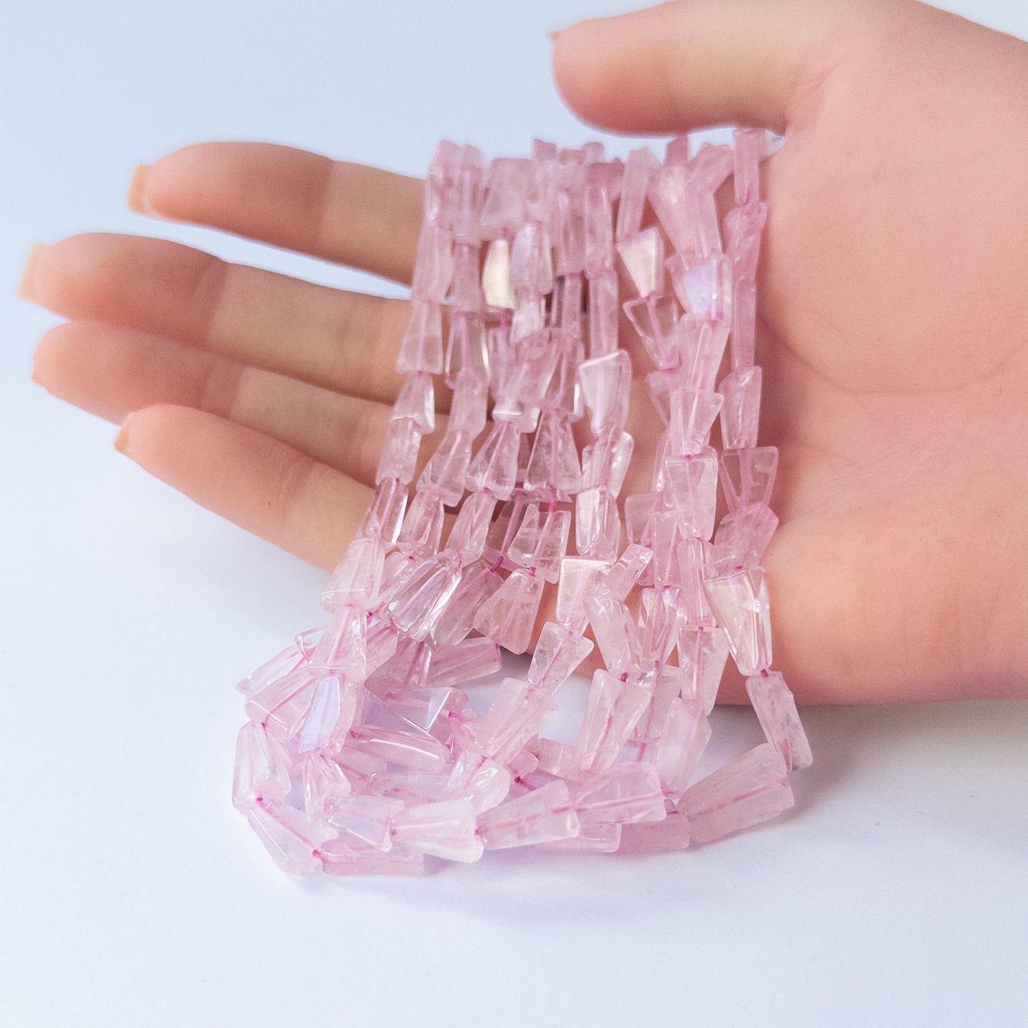 A person holds delicate strands of Rose Quartz tapered rectangle beads, showcasing their smooth design.