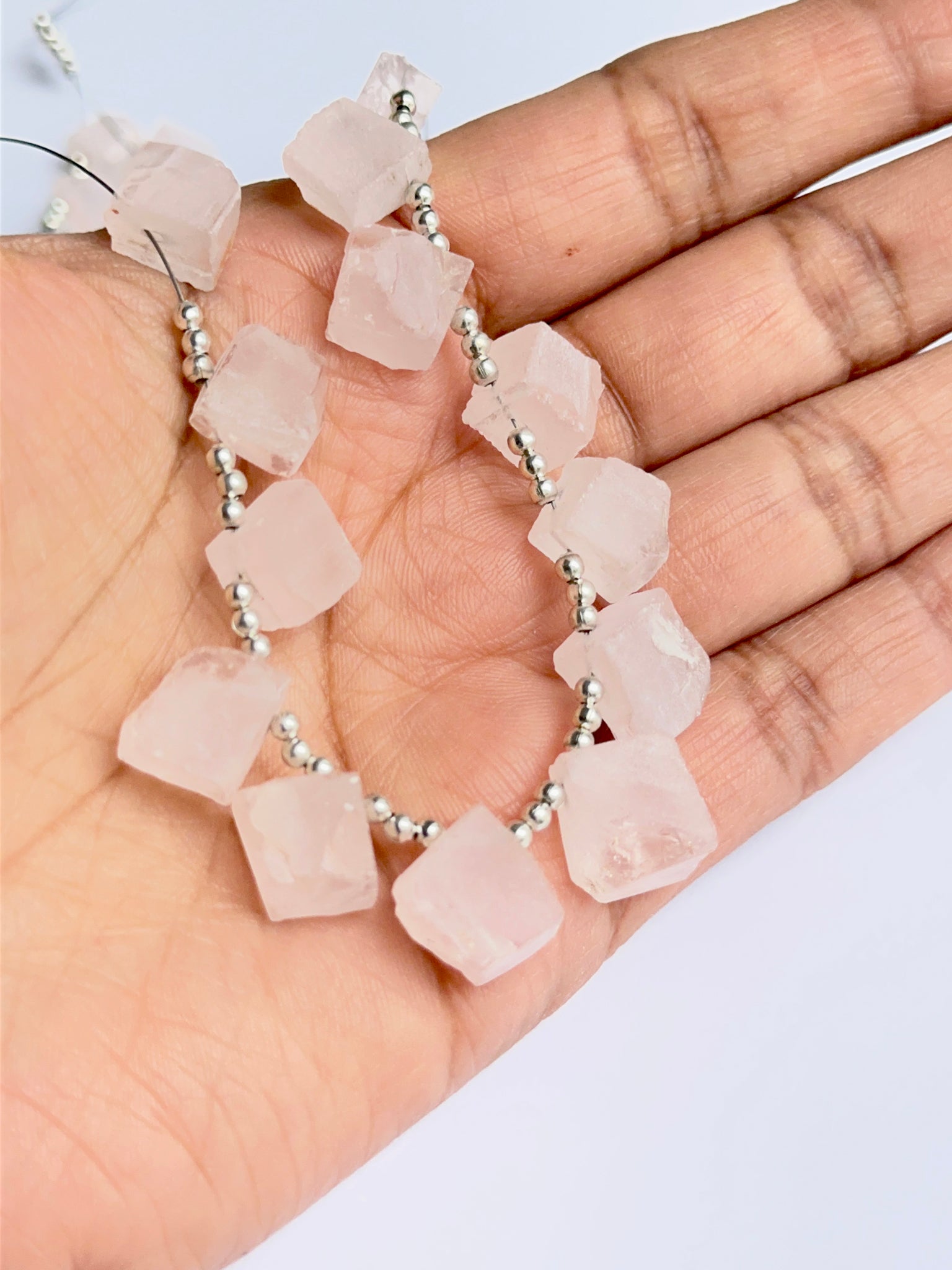 A person holds delicate strands of rose quartz rough beads, showcasing their smooth design.