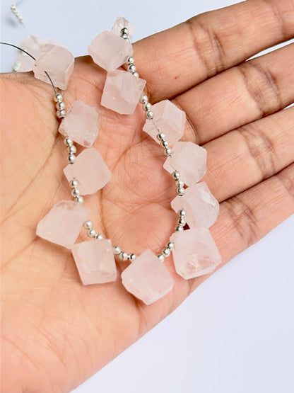 A person holds delicate strands of rose quartz rough beads, showcasing their smooth design.