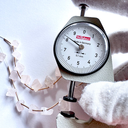 A dial gauge measures the Rose Quartz rough cut gemstone.