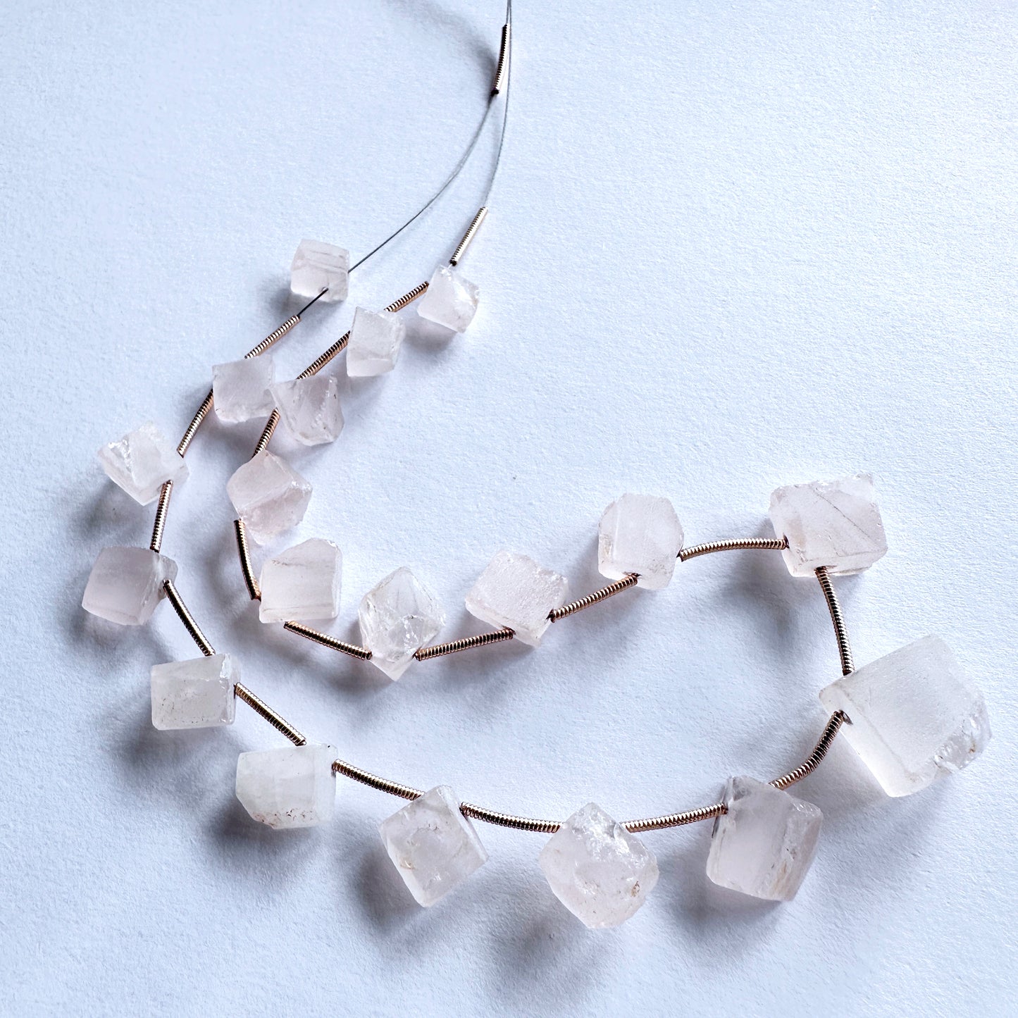 Smooth-cut Rose Quartz beads with subtle shine, laid out to display their organic shapes and quality.