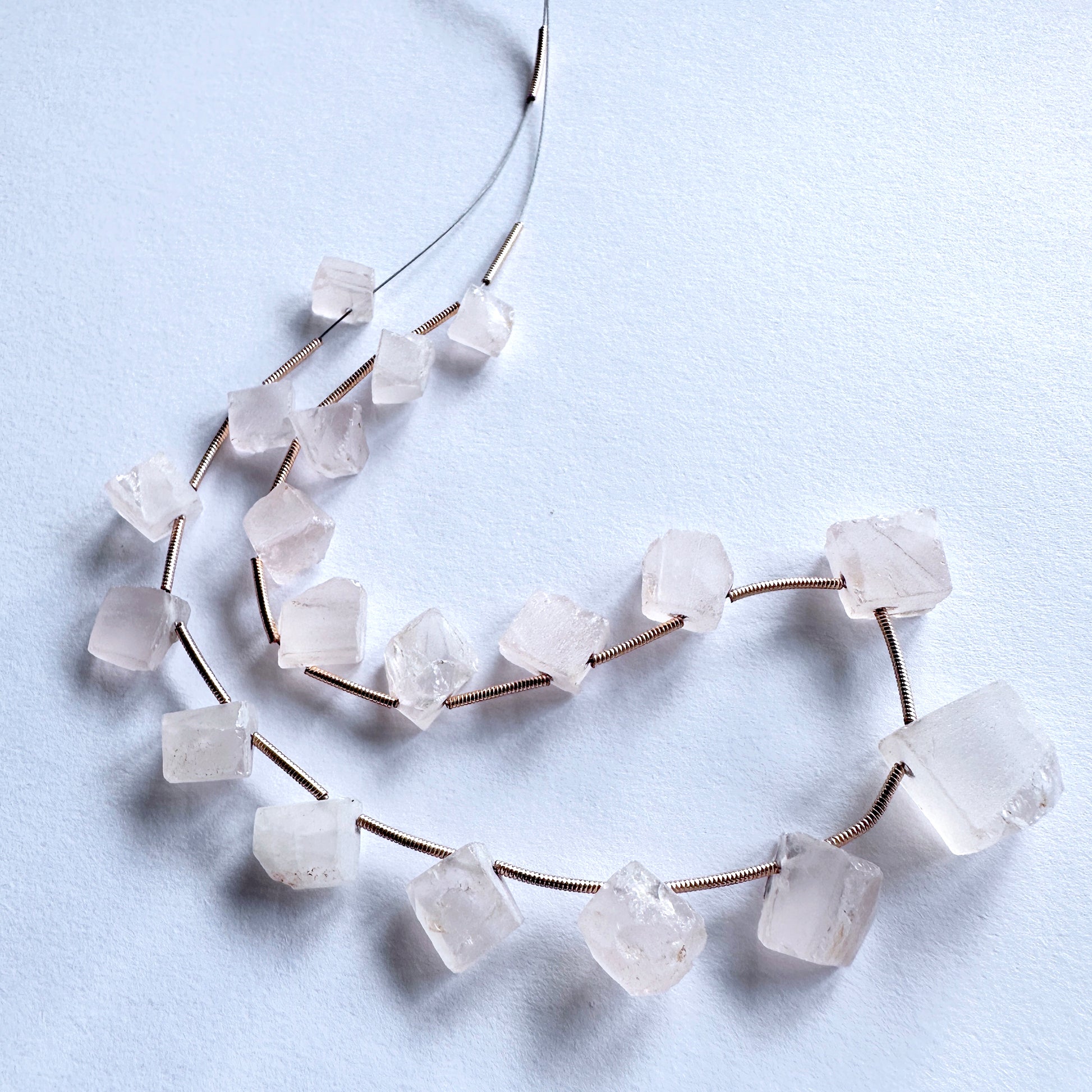 Smooth-cut Rose Quartz beads with subtle shine, laid out to display their organic shapes and quality.