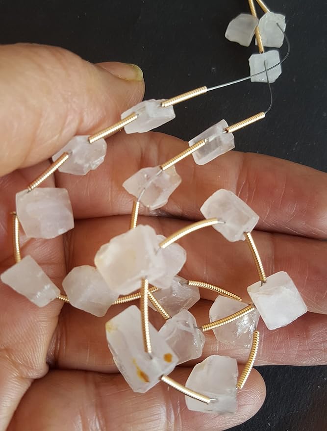 A person holds delicate strands of Rose Quartz beads.