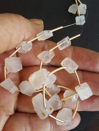 A person holds delicate strands of Rose Quartz beads.