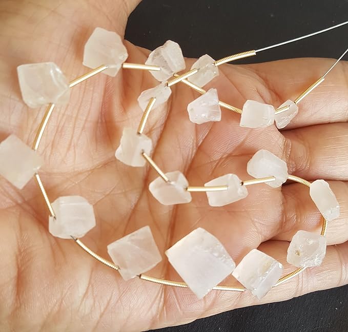 A person holds delicate strands of Rose Quartz beads,