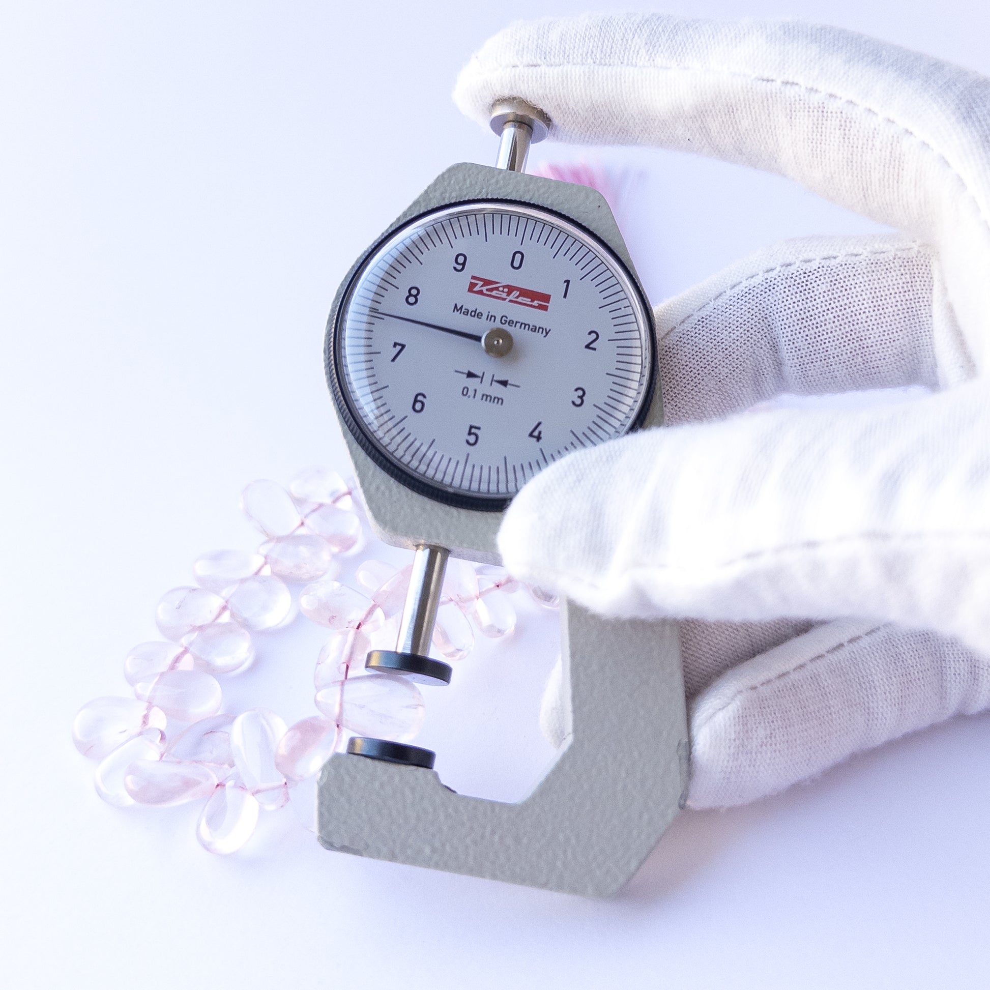A dial gauge measures the Rose Quartz smooth briolette 7–8.5mm gemstone.