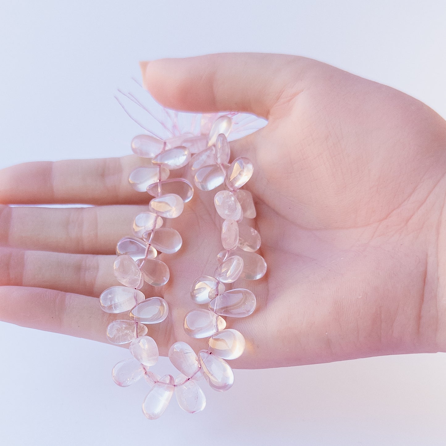 A person holds delicate strands of Rose Quartz beads, showcasing their smooth briolette design.