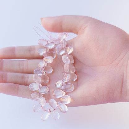 A person holds delicate strands of Rose Quartz beads, showcasing their smooth briolette design.