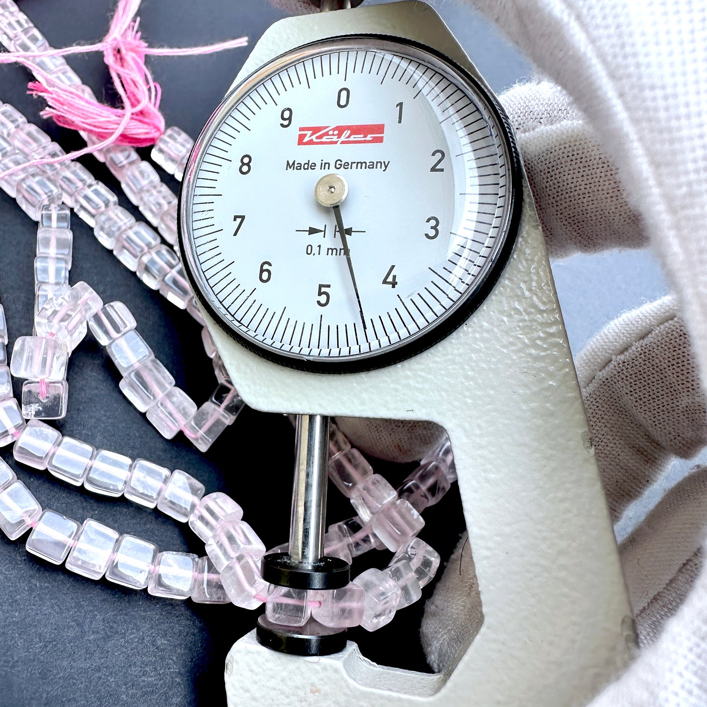 A dial gauge measures the Rose Quartz smooth square 5mm gemstone.