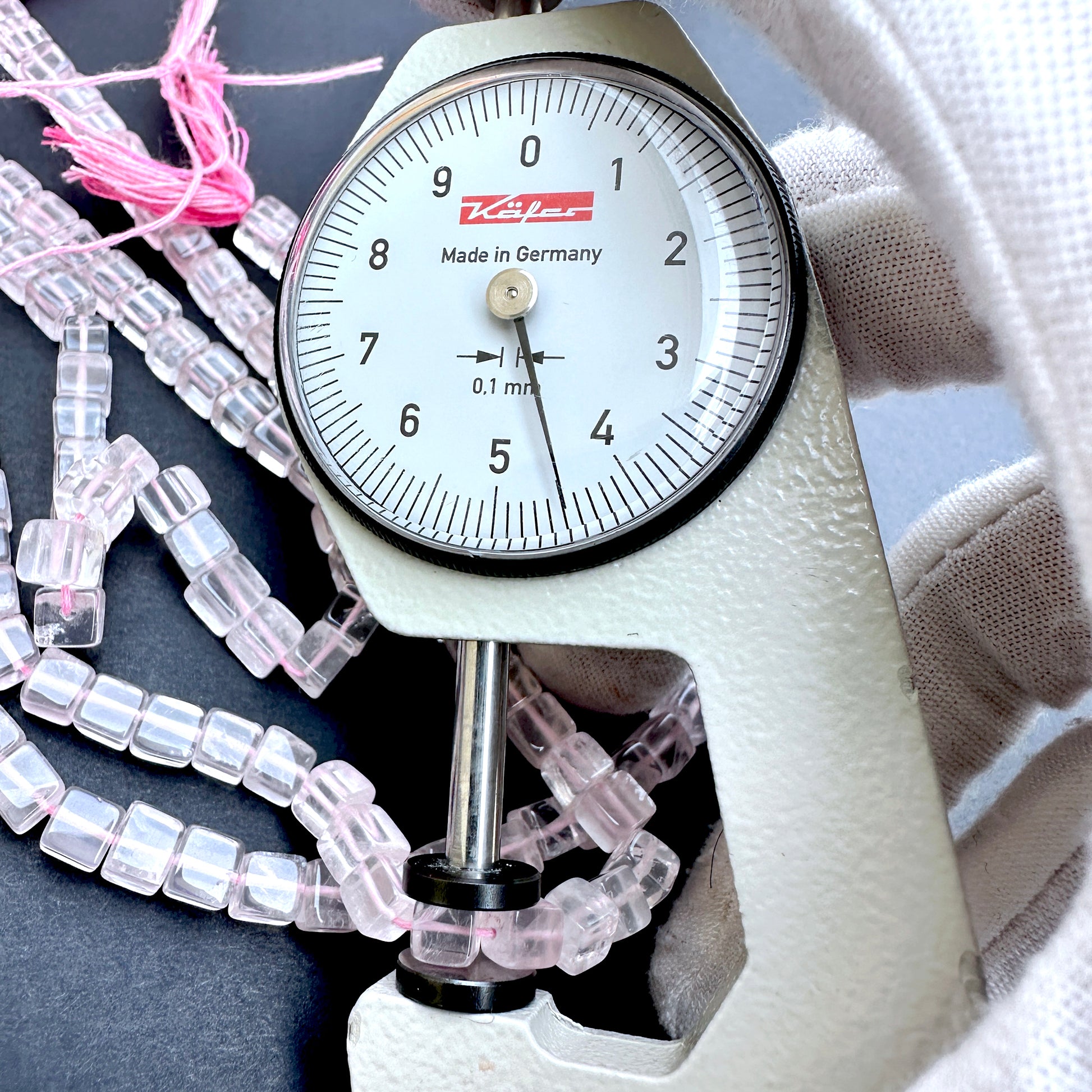 A dial gauge measures the Rose Quartz smooth square 5mm gemstone.