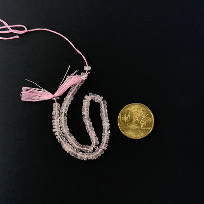 A coin is place near delicate strands of Rose Quartz beads for scale.