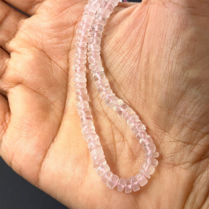 A person holds delicate strands of Rose Quartz beads, showcasing their smooth wheel design.