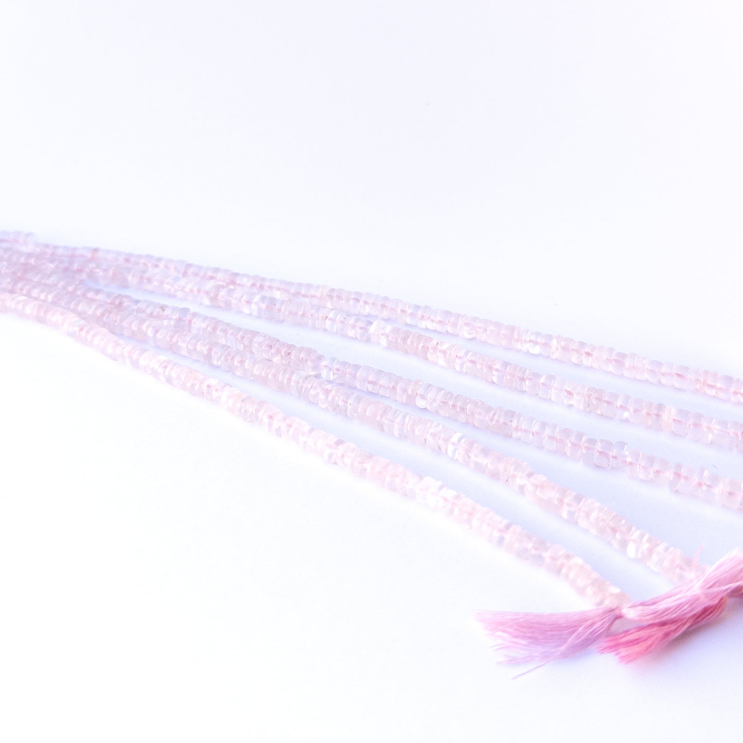 A person holds delicate strands of Rose Quartz beads, showcasing their smooth wheel design.